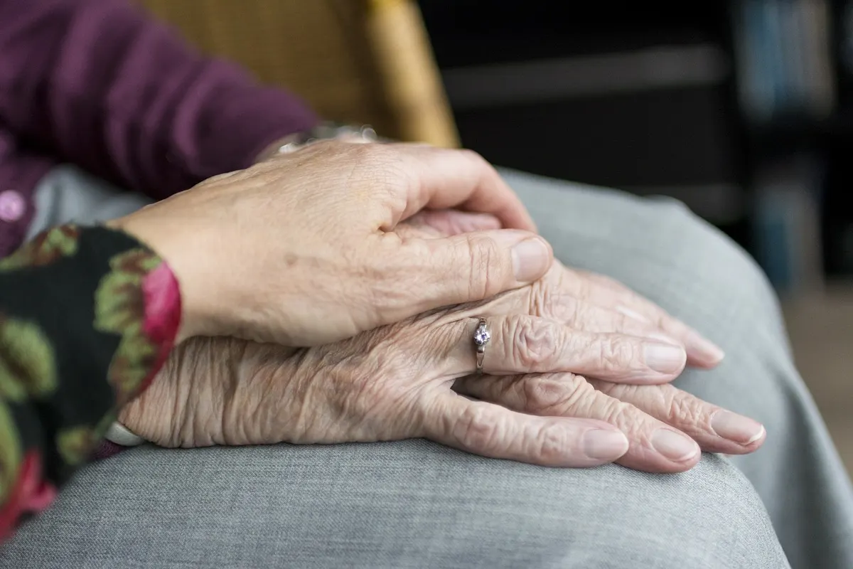 Hände einer Betreuungskraft und einer Seniorin